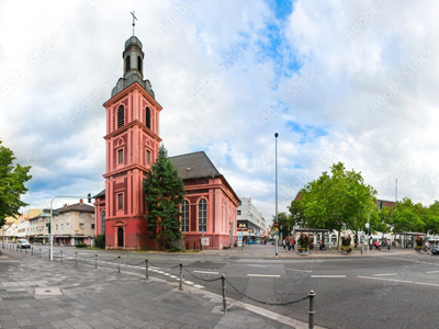 Kirche an einer Straßenecke mit Bäumen und Wolken im Hintergrund.