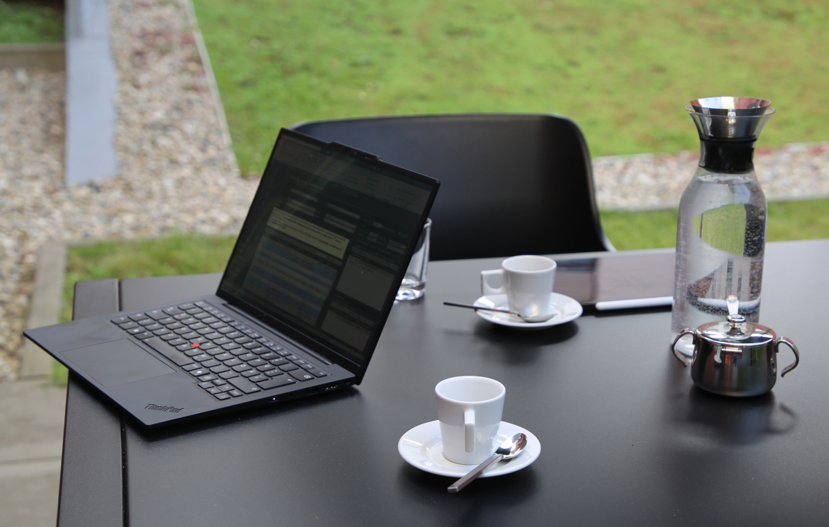 Ein Laptop, zwei Kaffeetassen, ein Wasserkrug, ein Teekännchen und ein Tablet auf einem Tisch.