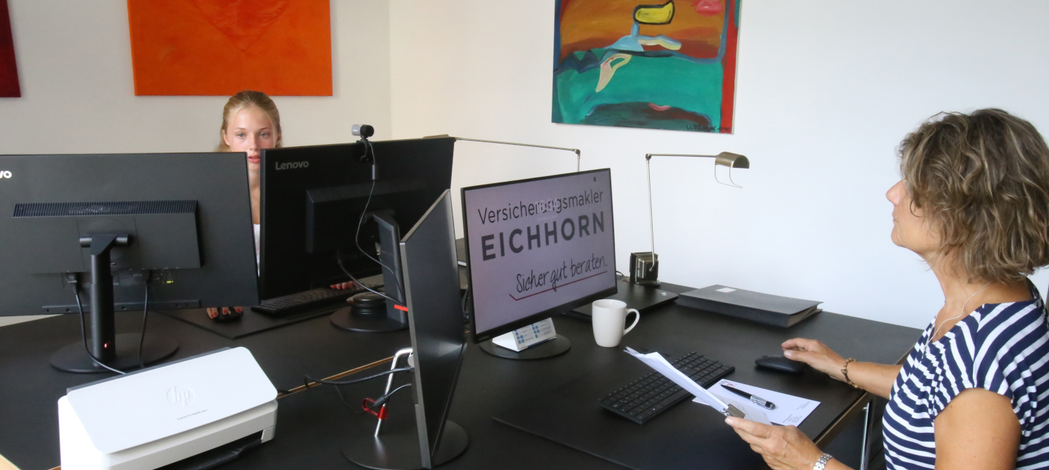 Zwei Frauen in einem modernen Büro, die an Computern arbeiten. Ein Monitor zeigt den Schriftzug „Versicherungsmakler EICHHORN – Sicher gut beraten“.